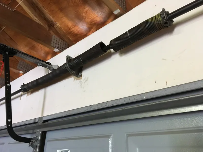 Broken torsion spring with a visible gap, next to the opener rail