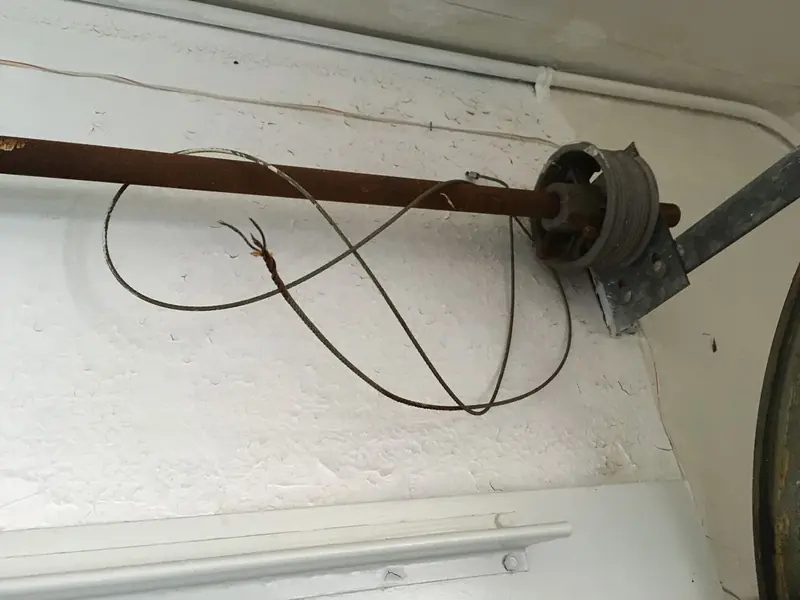 Snapped, frayed lift cable tangled near the cable drum above a garage door